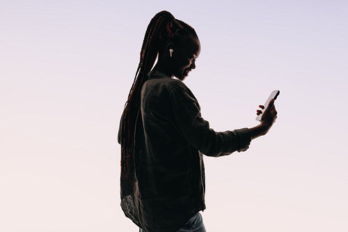 Confident woman smiling while video chatting on smartphone against white studio background