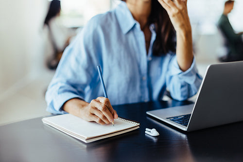 Woman writing notes during a phone call in an office