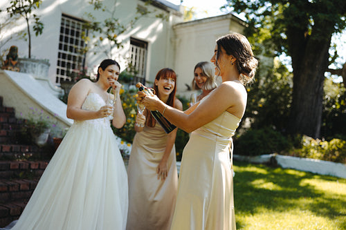 Bride and bridesmaids celebrating outdoors with champagne during a sunny wedding day