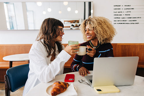 Friends clinking coffee mugs in a bright cafe