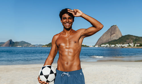 Smiling man on a beach holding a soccer ball under summer skies