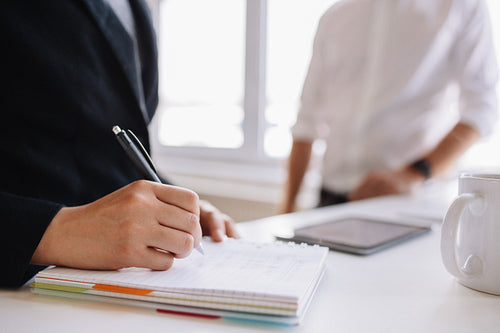 Woman taking notes with male colleague in background