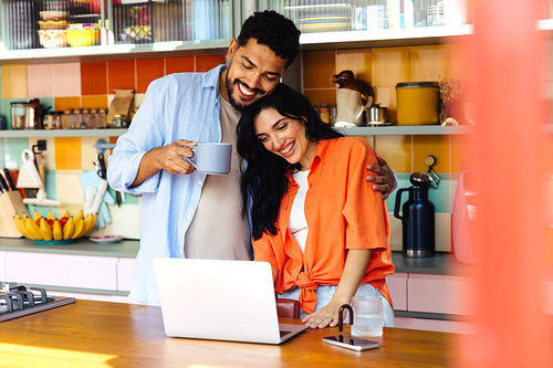 Happy couple smiling together using a laptop in a colorful kitchen