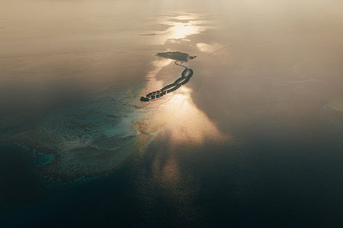 Drone view of a tropical island and calm ocean in the Maldives at sunset