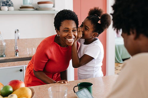 Daughter whispering to her mom in the kitchen at home