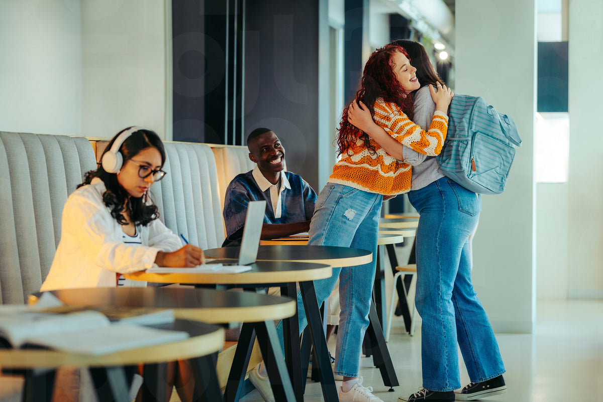 University friends greeting with a warm hug in a modern study area as ...