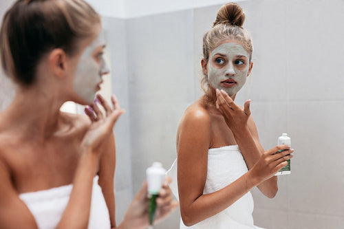 Woman applying mask cream on face in bathroom
