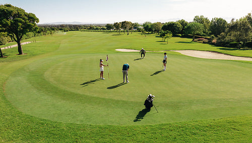 Golf group playing golf from the green at a sunny golf course surrounded by sand bunkers