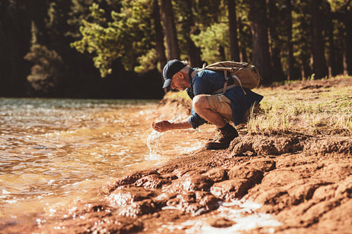 Mature man washing face from lake water