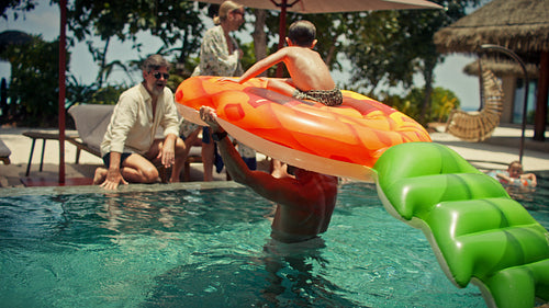 Family enjoys tropical vacation with pineapple inflatable float in swimming pool