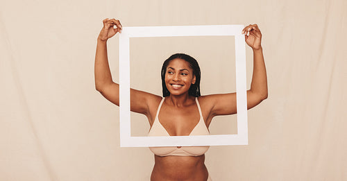 Cheerful young woman looking through a picture frame in a studio