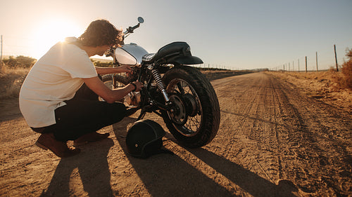 Man checking his motorcycle on country road