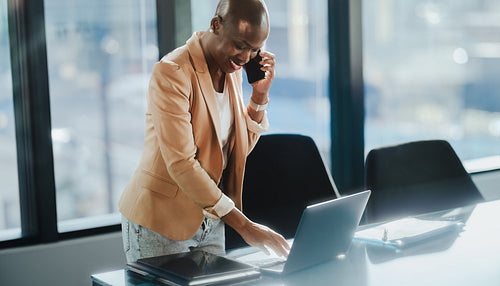 Businesswoman discussing company success on phone while standing at office desk