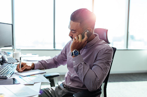 Businessman talking over mobile phone sitting at his office desk.