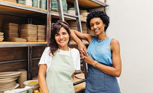Happy female potters smiling at the camera in their workshop