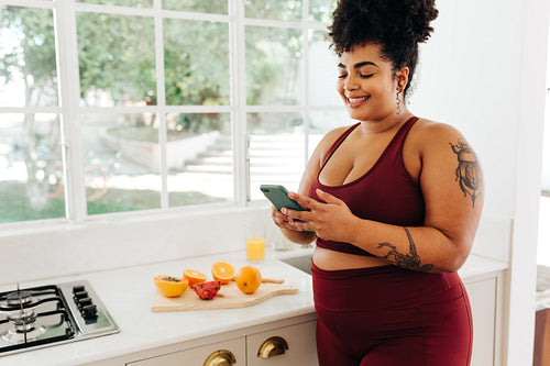 Happy fitness woman in kitchen using smart phone