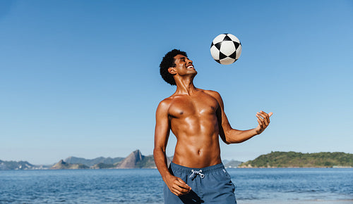 Young shirtless man joyfully playing with a soccer ball at the beach