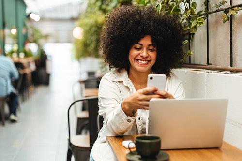 Happy young woman using a smartphone for online chatting in a coffee shop
