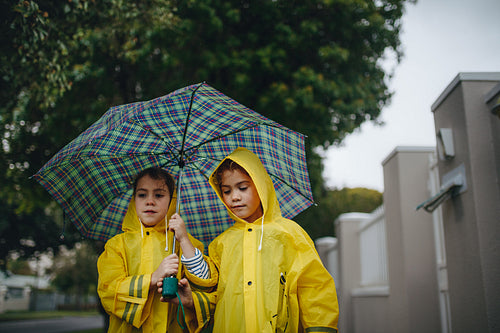 Two little girls with umbrella outdoors on rainy day