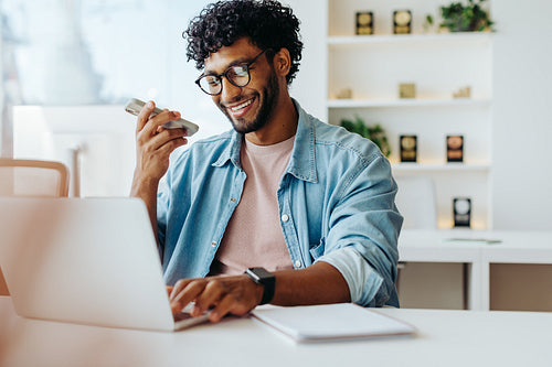 Young businessman using smartphone and laptop at office desk