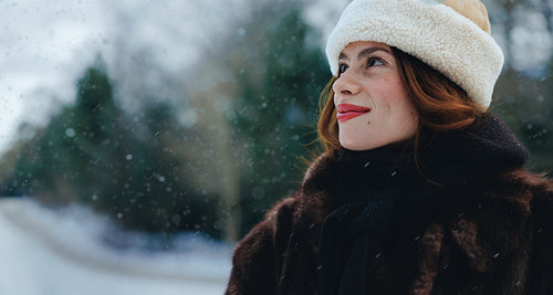 Woman looks upward at falling snow in a winter hat