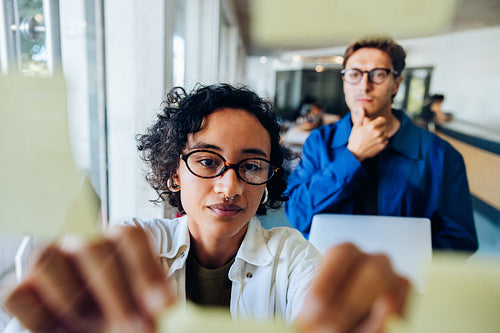 Woman pins notes while man analyzes ideas