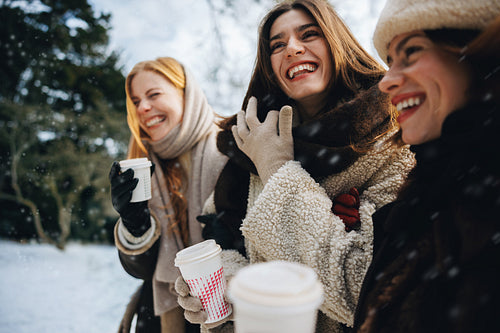Women friends laugh over hot chocolate in winter snow