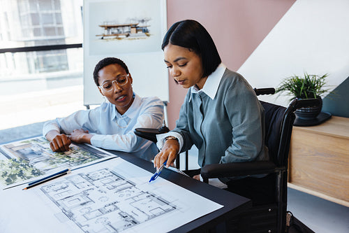 Two women discussing architectural plans in a modern workspace.