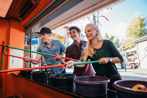 Friends having fun with fishing game in amusement park