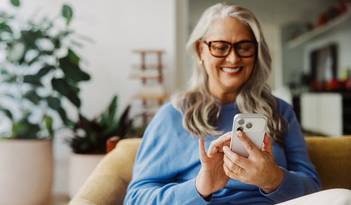 Senior woman taps a smartphone on the sofa at home
