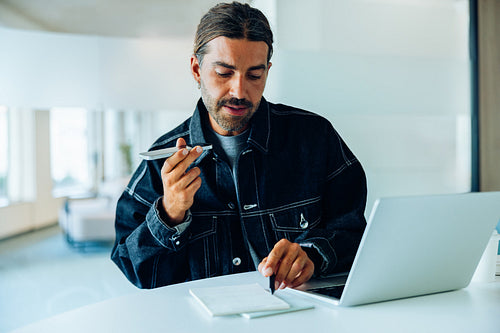 Man using laptop and writing notes in denim jacket
