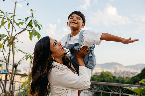 Mother lifts happy child outdoors with a city view in the background