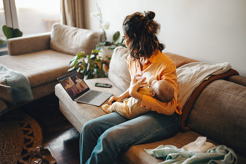 Mother feeds baby during virtual meeting at home
