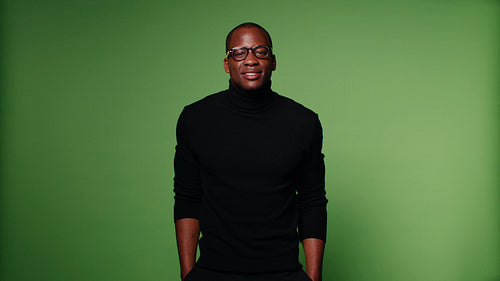 Confident man in a black turtleneck and glasses poses against a green screen