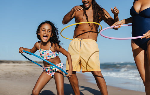 Joyful girl playing with hula hoop at the beach with family on a summer day