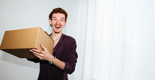 A package delivery moment with a young man holding a box indoors.