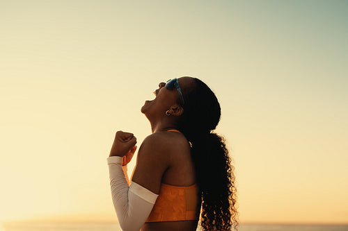 Victorious female athlete celebrating championship win on coastal beach at sunset