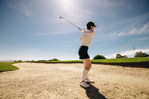 Sportswoman swinging golf club in sand in the sunshine