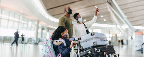 Young daughter and family with luggage trolley at airport