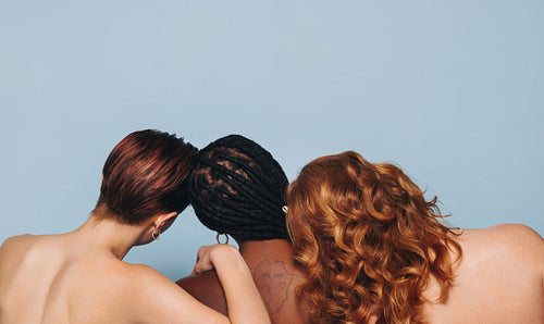 Rearview of three women with different skin tones standing together in a studio