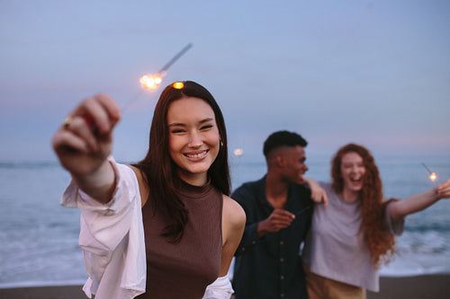 Cheerful young woman holding up a sparkling light at the beach