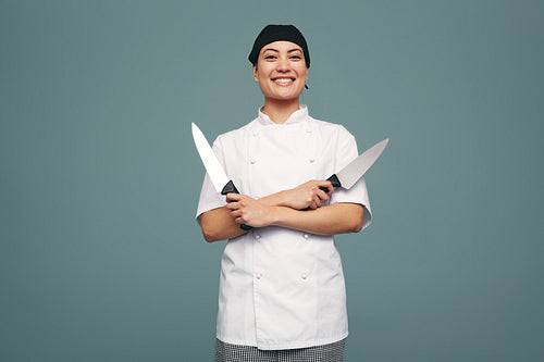 Happy culinary chef holding two knives in a studio
