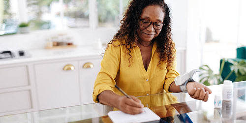 Woman with hypertension recording her blood pressure levels in her health journal