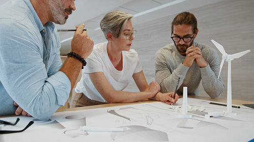 Creative business people designing a wind turbine using blueprints and 3D models in a team collaboration