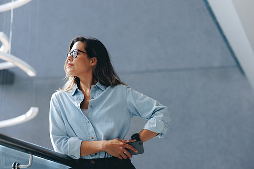 Business woman thinking as she stands in an office with a phone in her hand