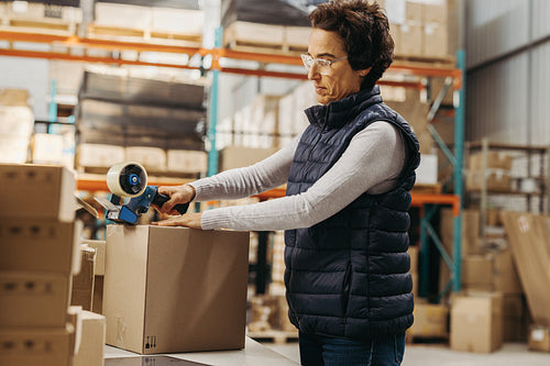 Warehouse worker taping a cardboard box with scotch tape