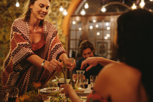 Woman serving food to friends at dinner party
