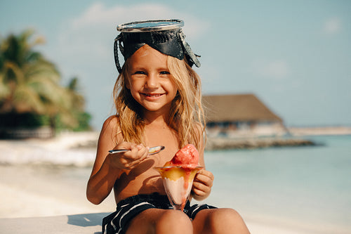 Young boy enjoying ice cream on a tropical island trip, wearing a snorkel mask