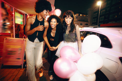 Three joyful friends enjoying a night out holding balloons on the street