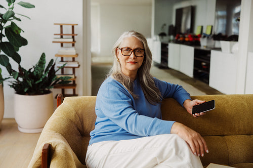 Seated senior uses a smartphone on a sofa at home